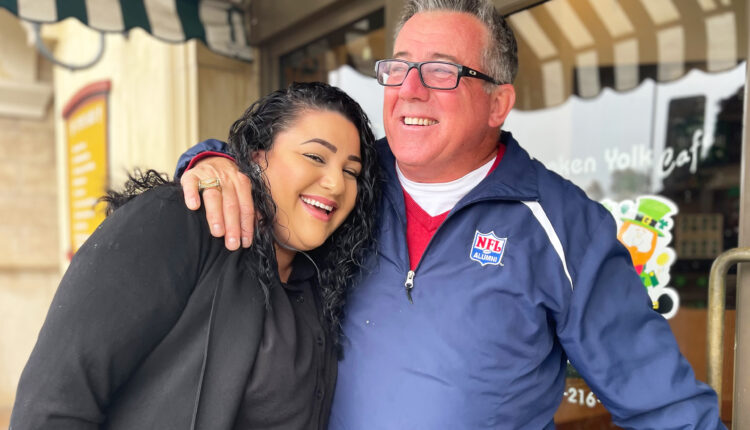 A photo of a man and a woman hugging outside of a restaurant.