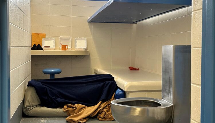 A photo of someone lying under a blanket in a jail cell.