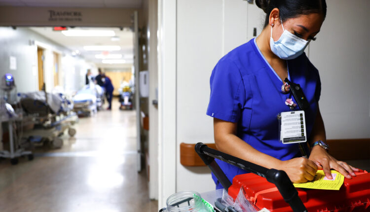 A photo of a lab technician writing a note while wearing a surgical mask and scrubs inside a hospital.
