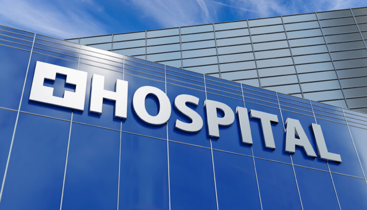 On the side of a hospital building, a large sign reads "HOSPITAL" under blue sky.