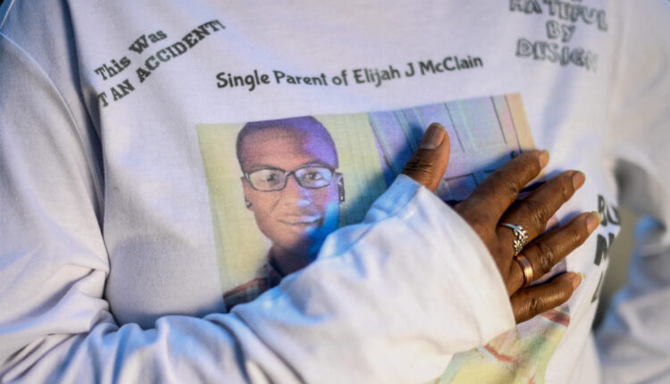 A closeup image of a woman's torso wearing a sweatshirt printed with the photo of a young man and lines of text, including one that reads "Single Parent of Elijah J Mclain".
