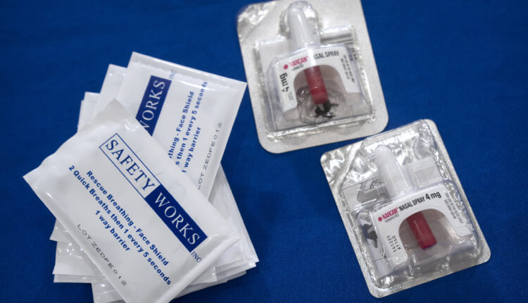 Two containers of Narcan and a small stack of packages that say, "SAFETY WORKS" are on a blue table.