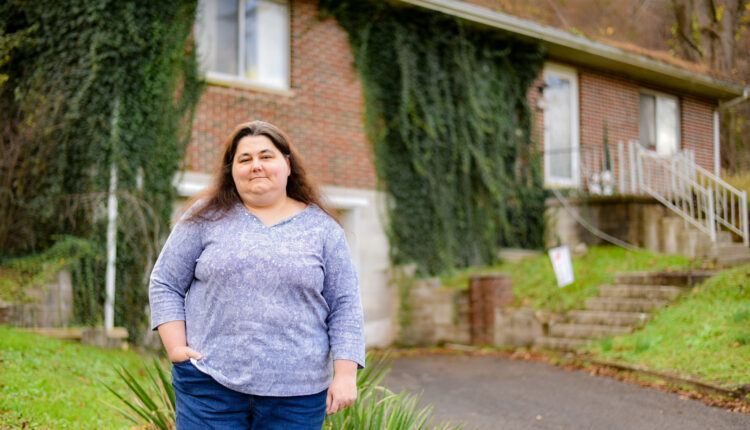 A photo of a woman standing for a portrait outside of her house.