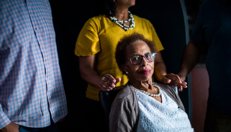 A photo of an elderly woman seated for a portrait with her adult daughter behind her.