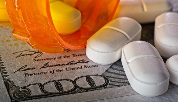 A photo of a 100-dollar bill with a medicine bottle spilling white pills onto it.