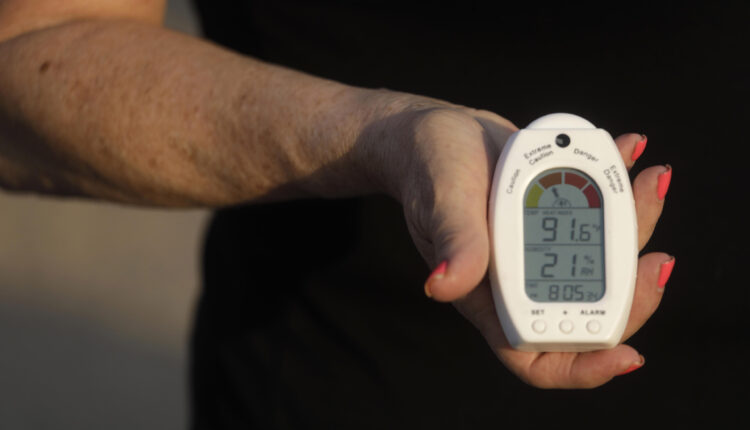 A woman holds a heat and humidity index device in her hand, facing towards the camera.