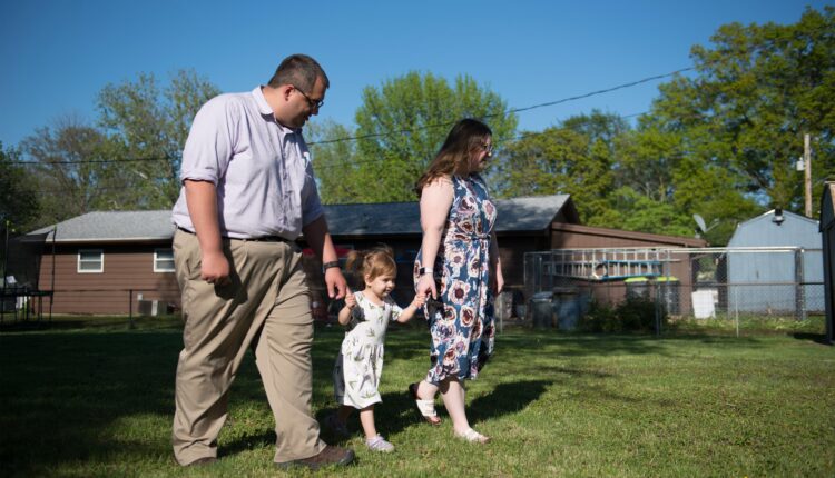 A photo of two parents walking with their young daughter outside.